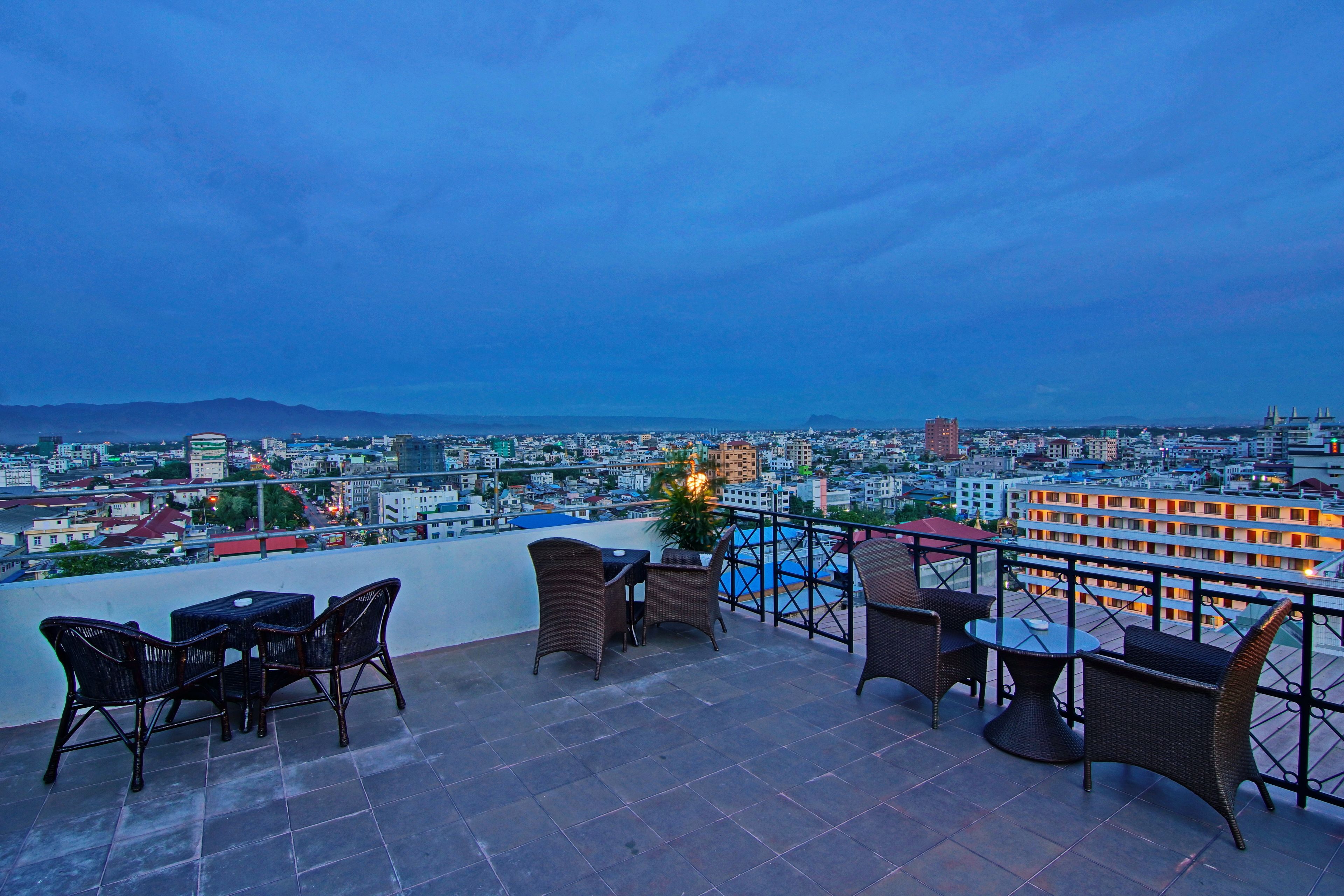A rooftop terrace with wicker furniture and a view of a cityscape at dusk.