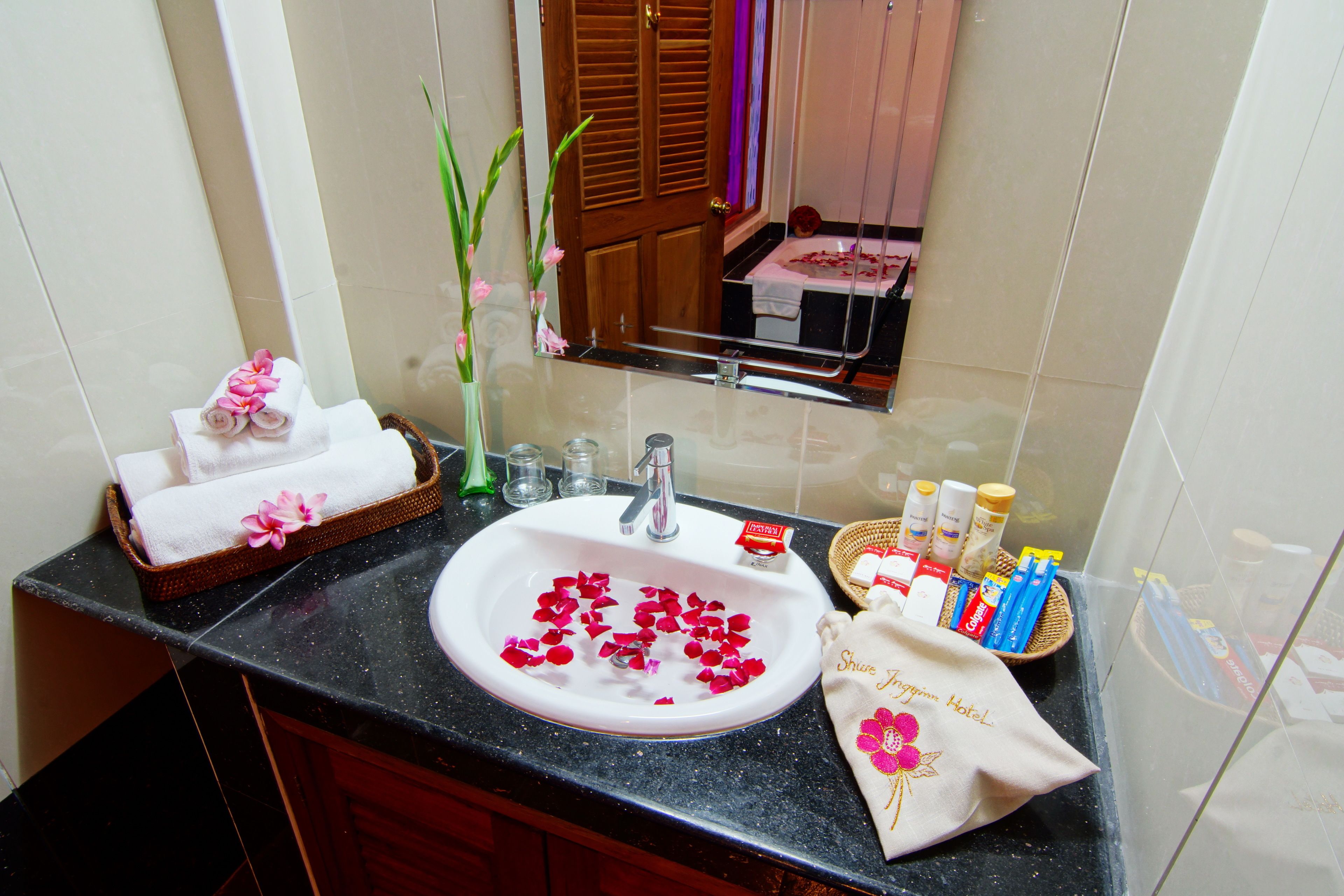 A bathroom with a sink, toiletries, a towel, and a vase with flowers.