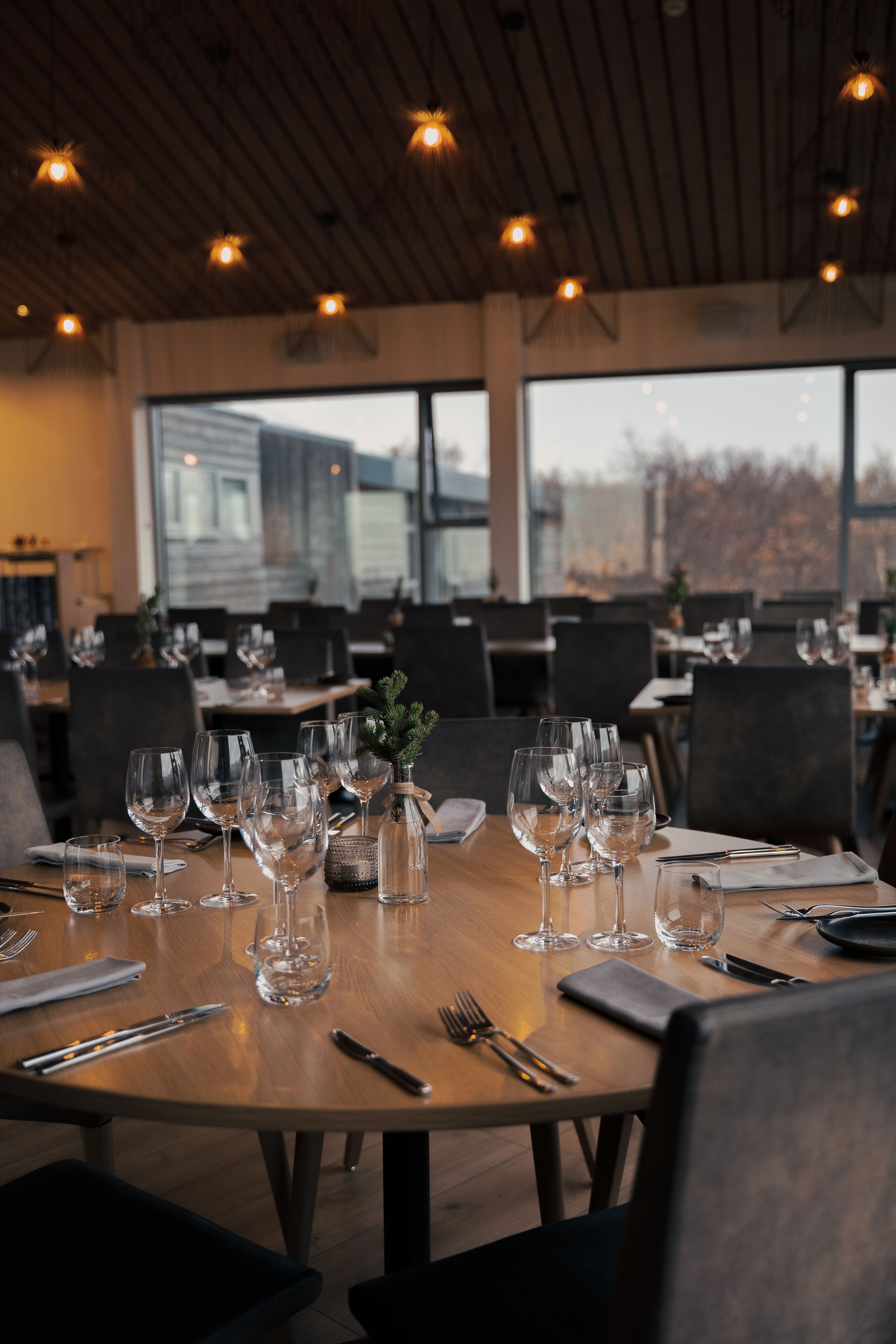 A restaurant with multiple tables set for dining, large windows, and a view of the outside.