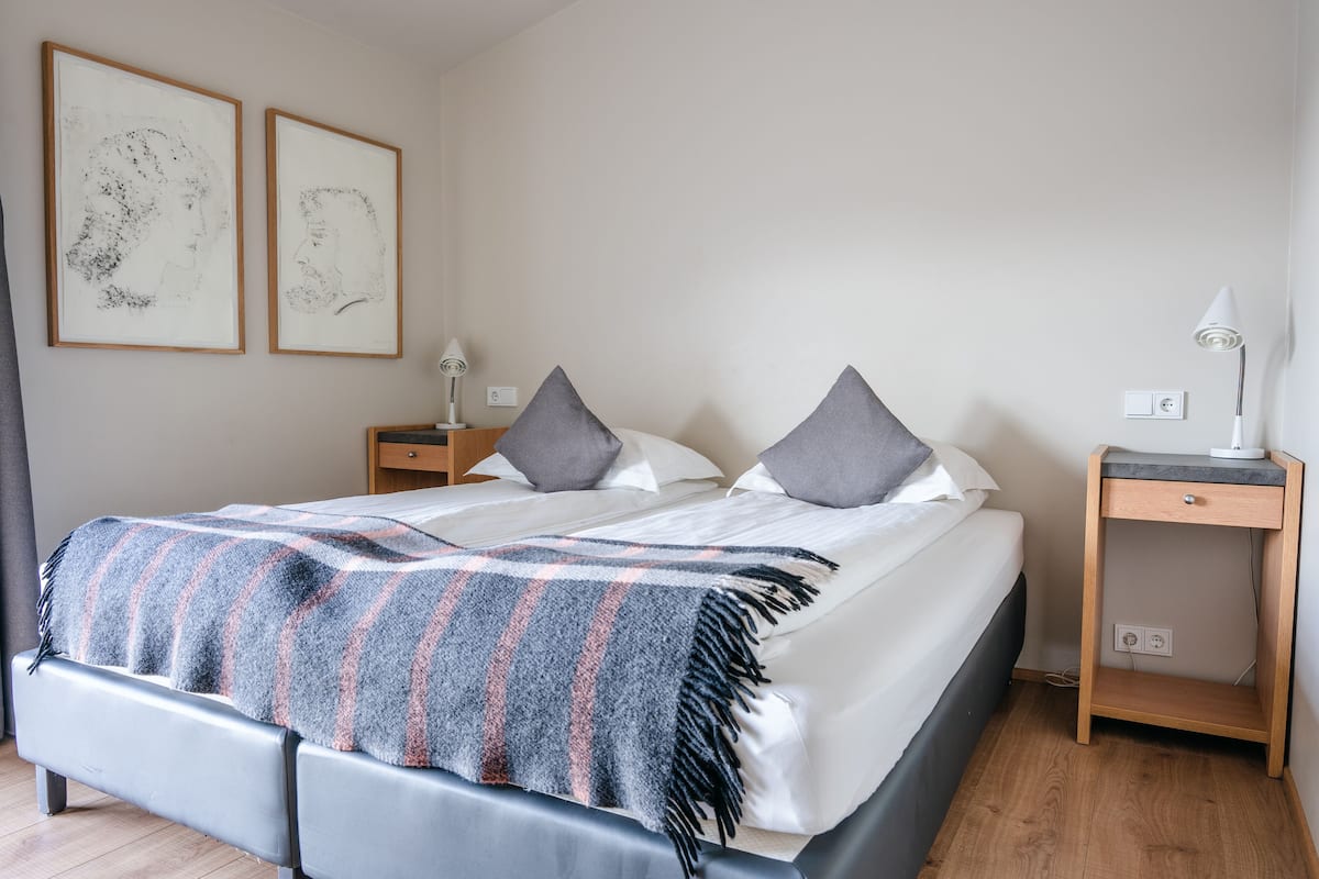 A neatly made bed with a striped blanket, two bedside tables with lamps, and two framed artworks on the wall.