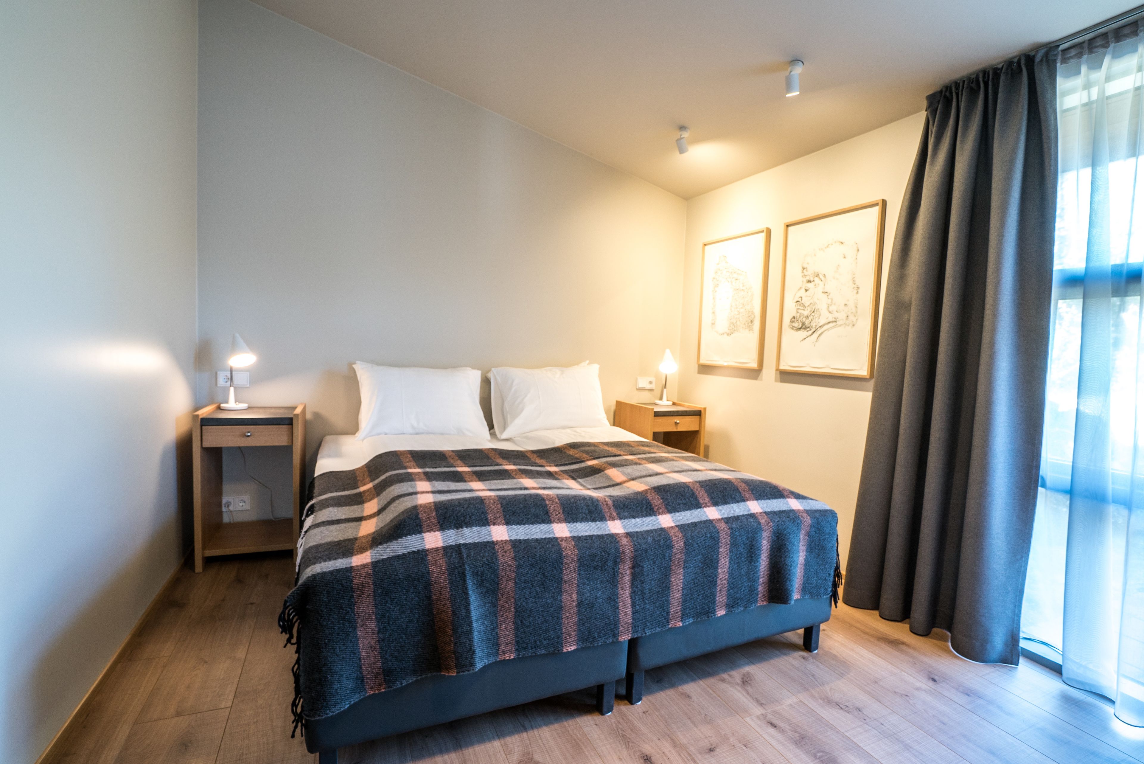 A modern bedroom with a large bed, two bedside tables, and a window with curtains.