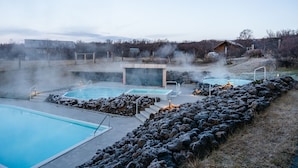 Ett geotermiskt spa med flera pooler, en bastu och en trähusliknande stuga i en naturskön miljö.