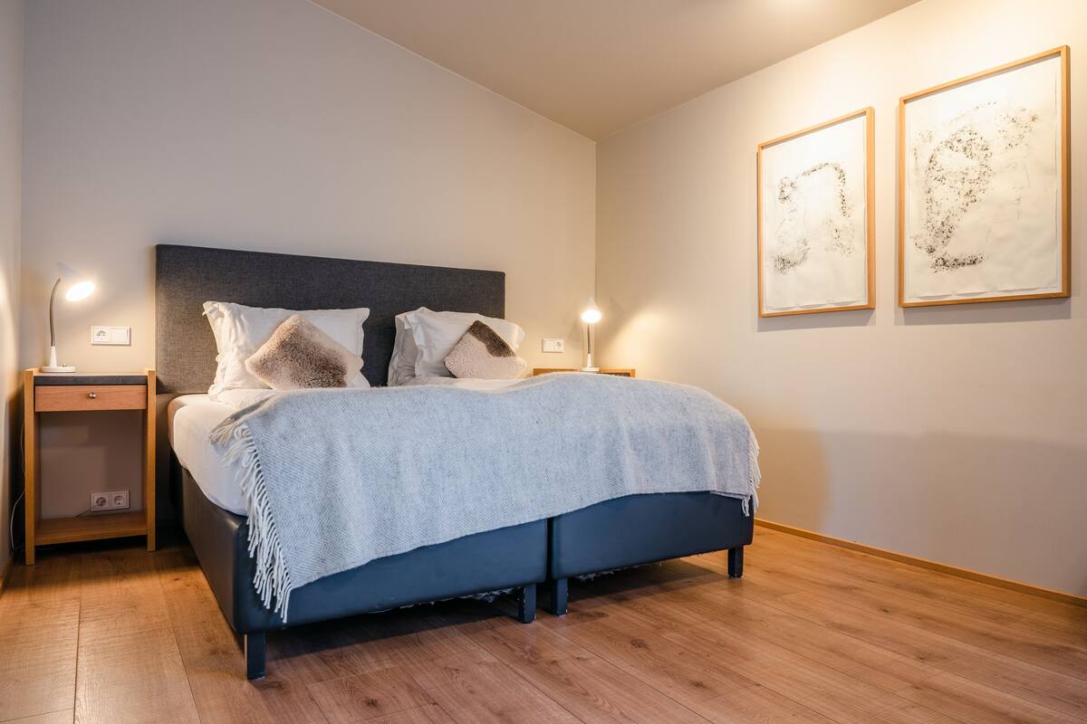 A modern bedroom with a dark blue bed, white bedding, and two wall-mounted lamps.