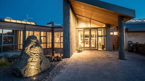 En modern byggnad med en stor stenskulptur framför, en överbyggd entré och en gång av tegelstenar.