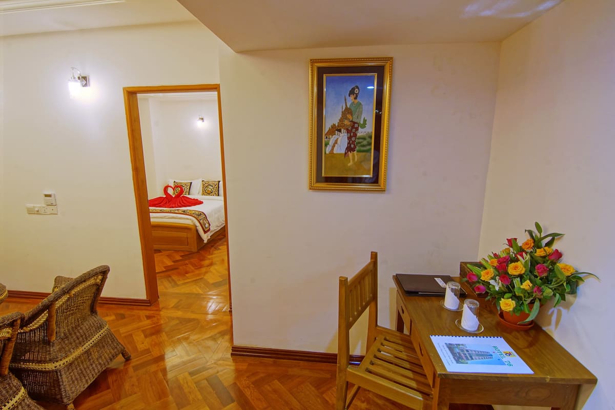 Ein Hotelzimmer mit Holzboden, einem Esstisch mit Stühlen, einem Laptop, einer Vase mit Blumen und einem gerahmten Bild an der Wand.