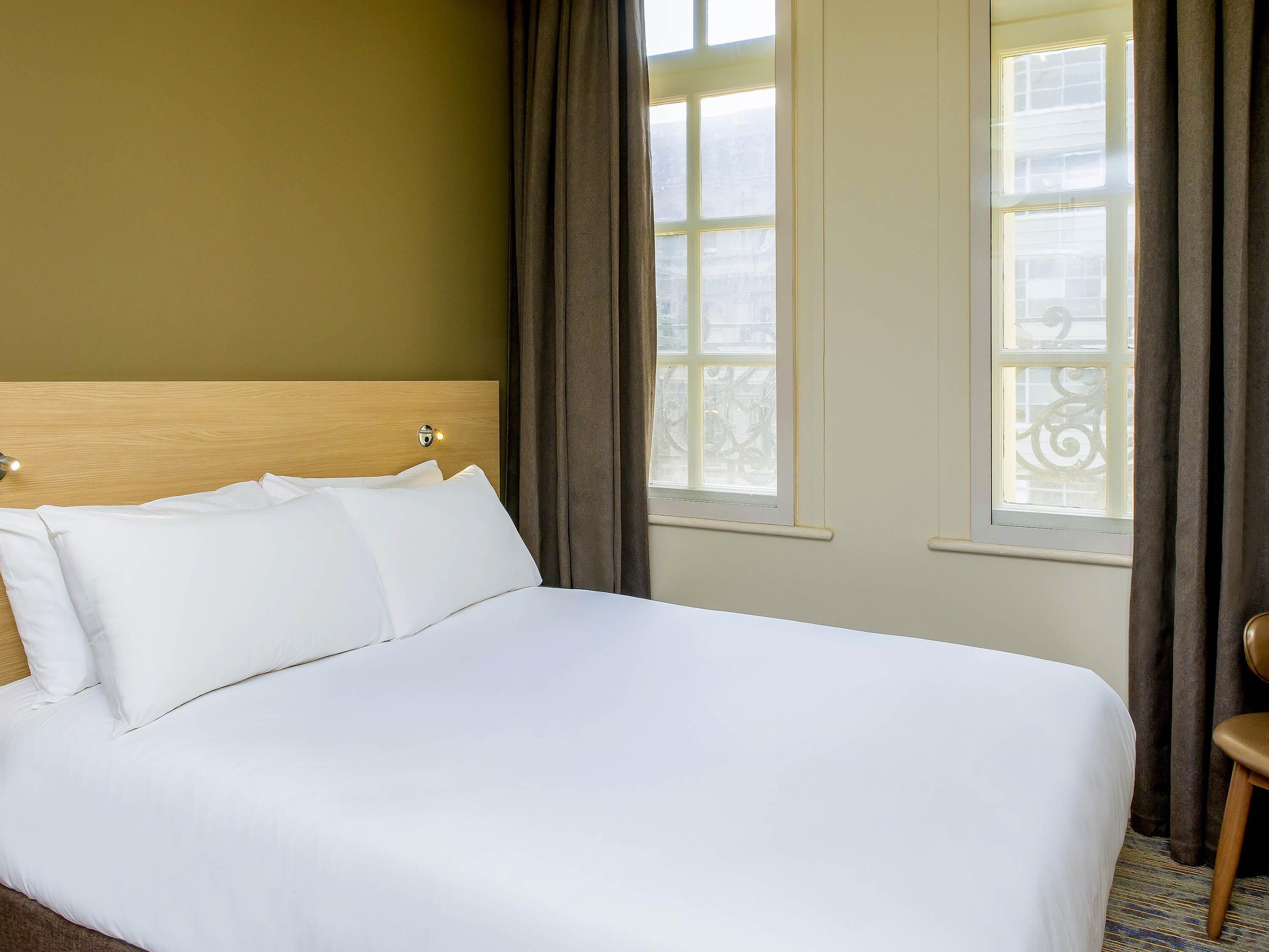 Een hotelkamer met een groot bed, een houten hoofdeinde en uitzicht op de stad.