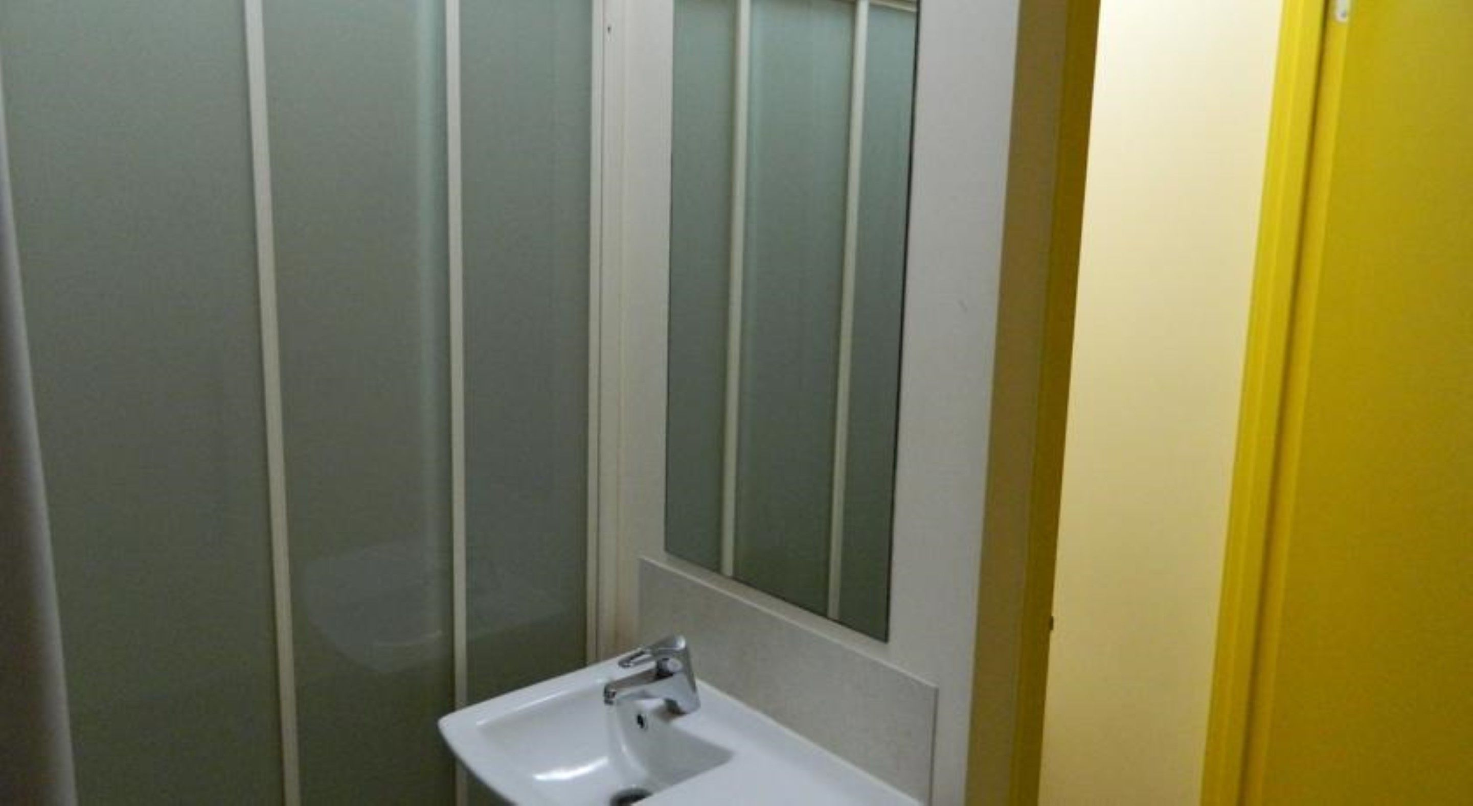 Un baño con lavamanos blanco, un espejo y paneles de vidrio esmerilado.