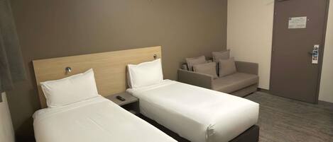 A hotel room with two single beds, a sofa, a nightstand, and a door with a lock.