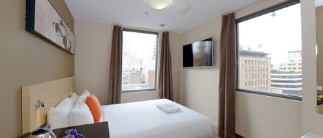 Hotelkamer met een bed, een flatscreen-tv, een raam met gordijnen, een koffiezetapparaat en een klein tafeltje met spullen.