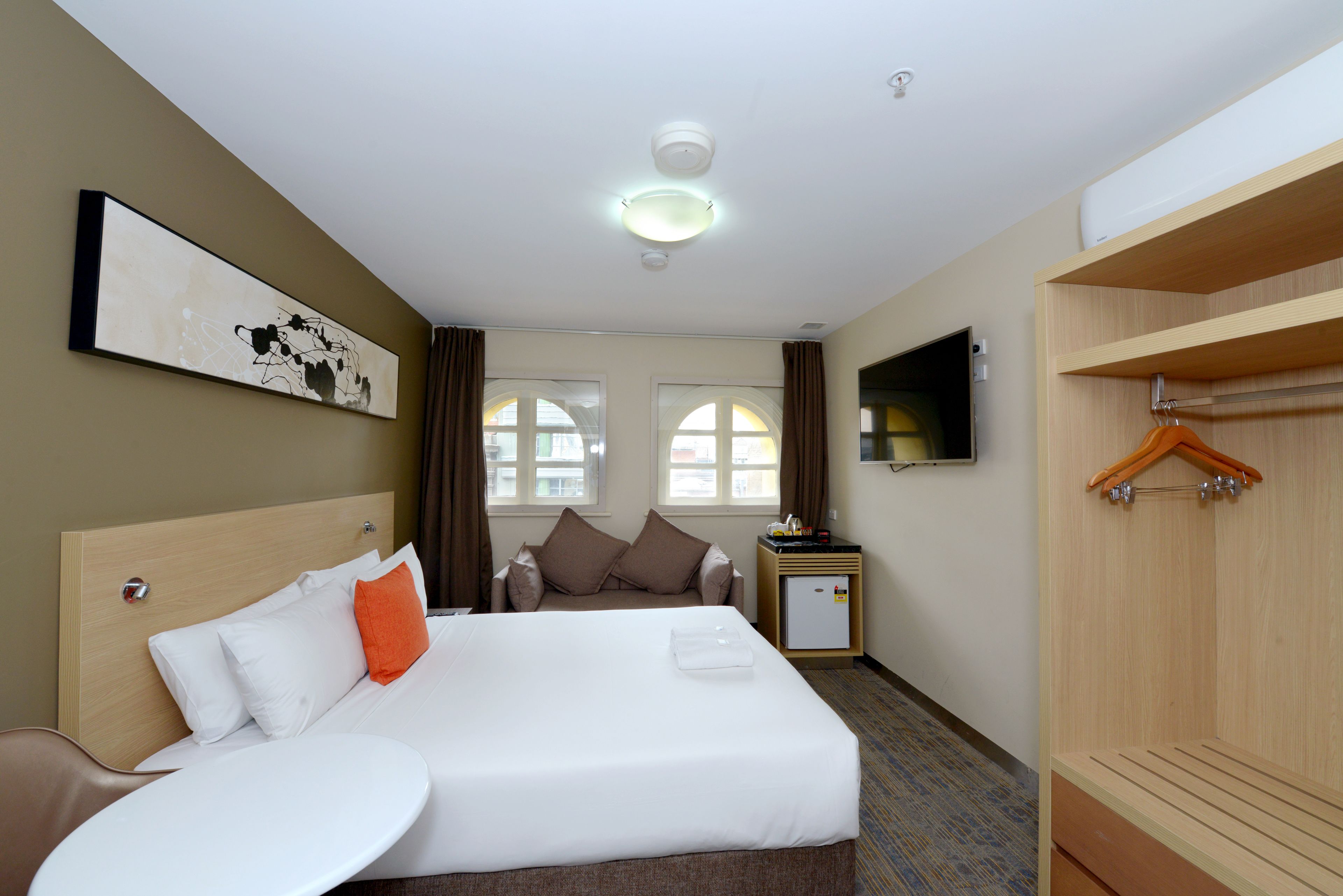 A hotel room with a bed, a small table, a TV, and a wardrobe.