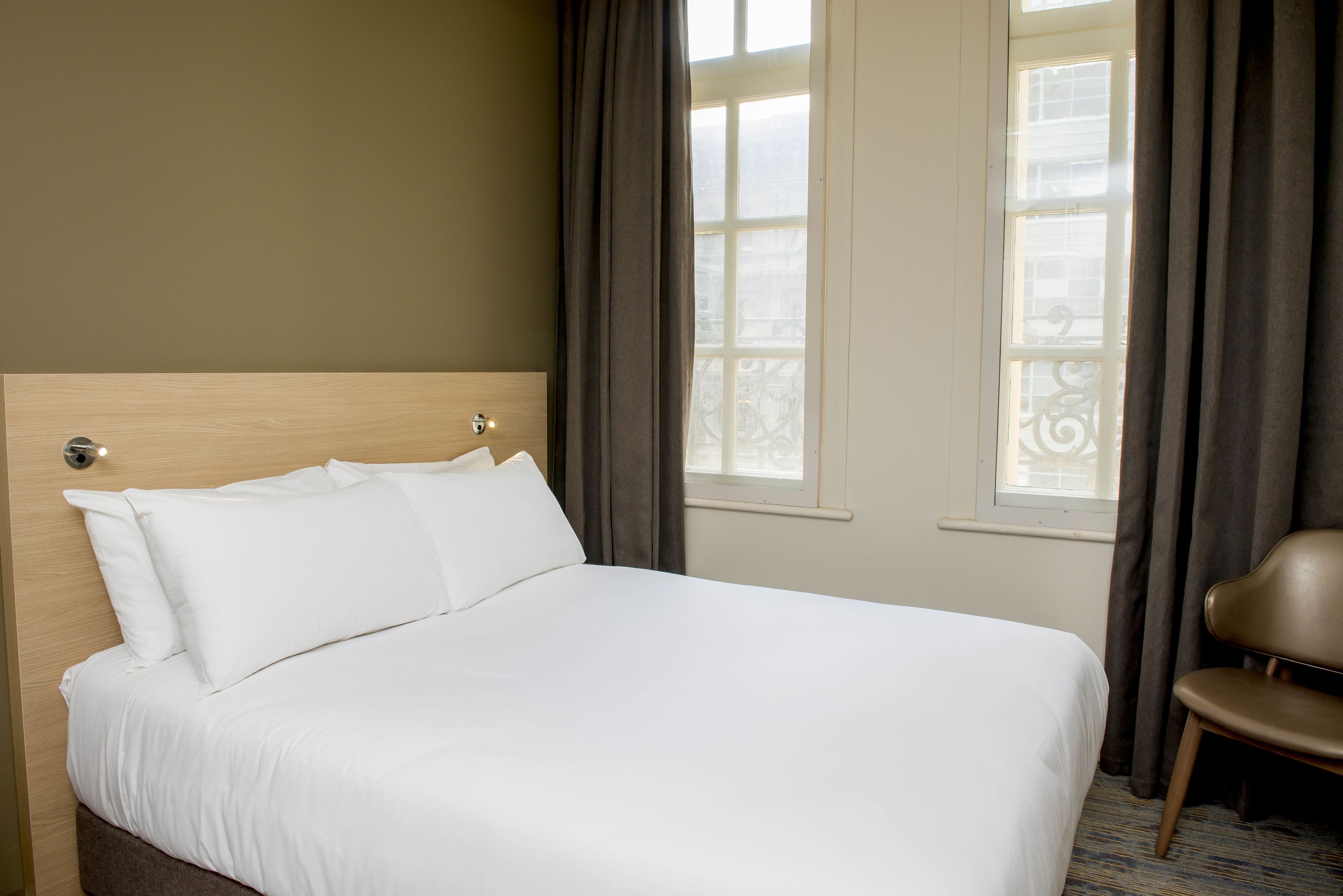 Een hotelkamer met een groot bed, een houten hoofdeinde en uitzicht op de stad.
