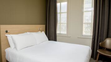 Une chambre d’hôtel avec un grand lit, une tête de lit en bois et une vue sur la ville par la fenêtre.
