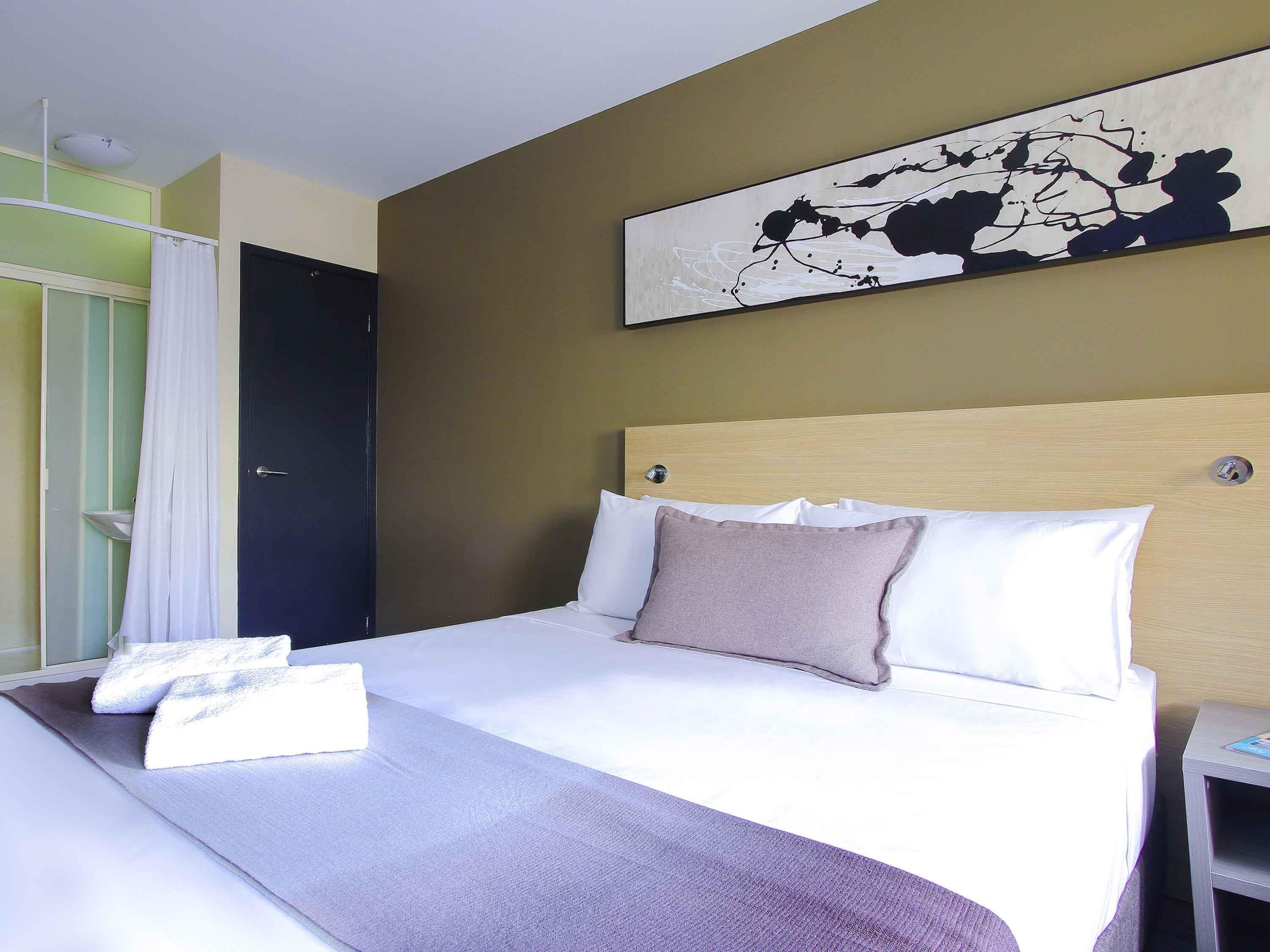 Ett hotellrum med en säng, en sänggavel, ett konstverk som hänger på väggen och ett badrum som syns genom en öppen dörr.