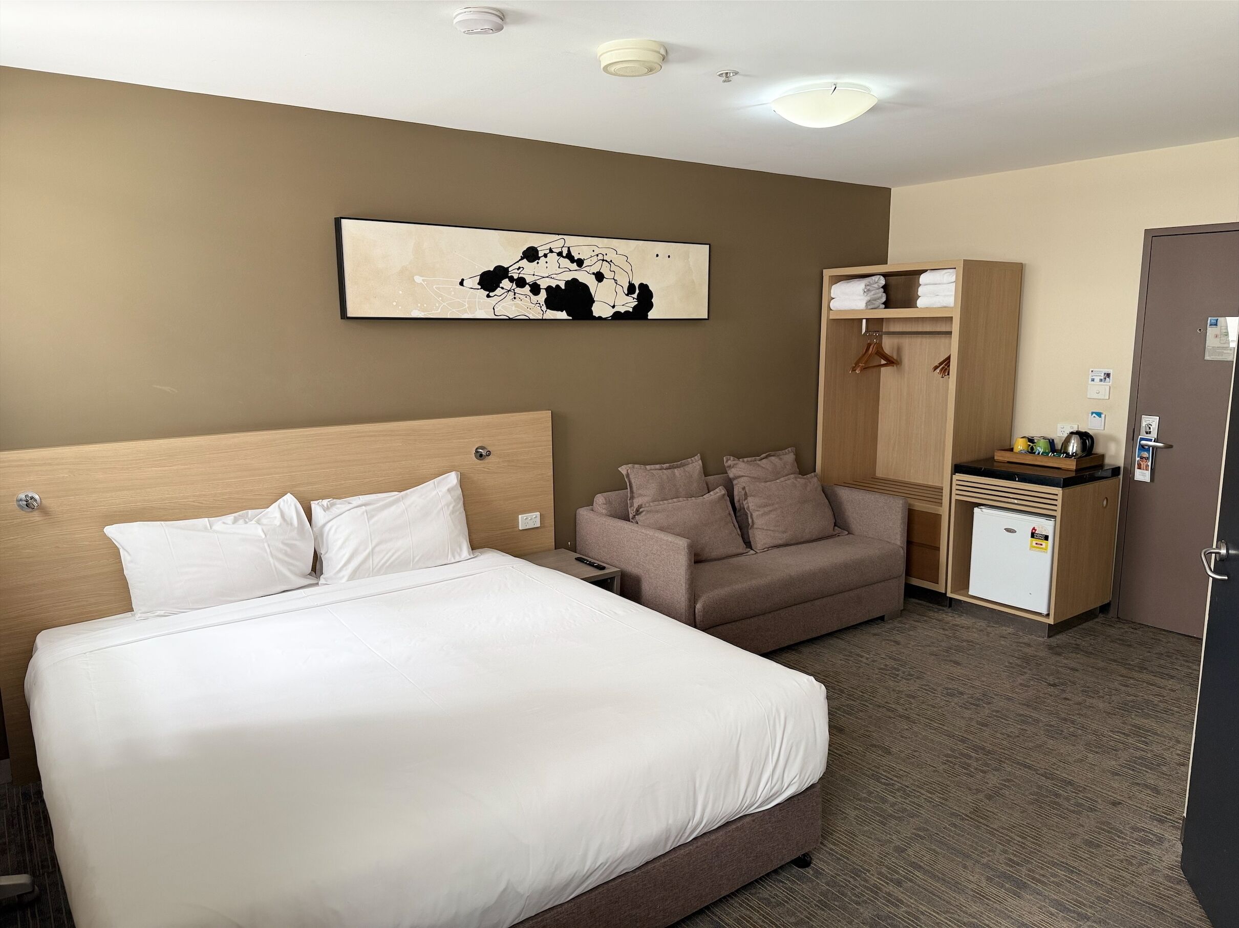 A hotel room with a large bed, a sofa, a small refrigerator, and a wardrobe.
