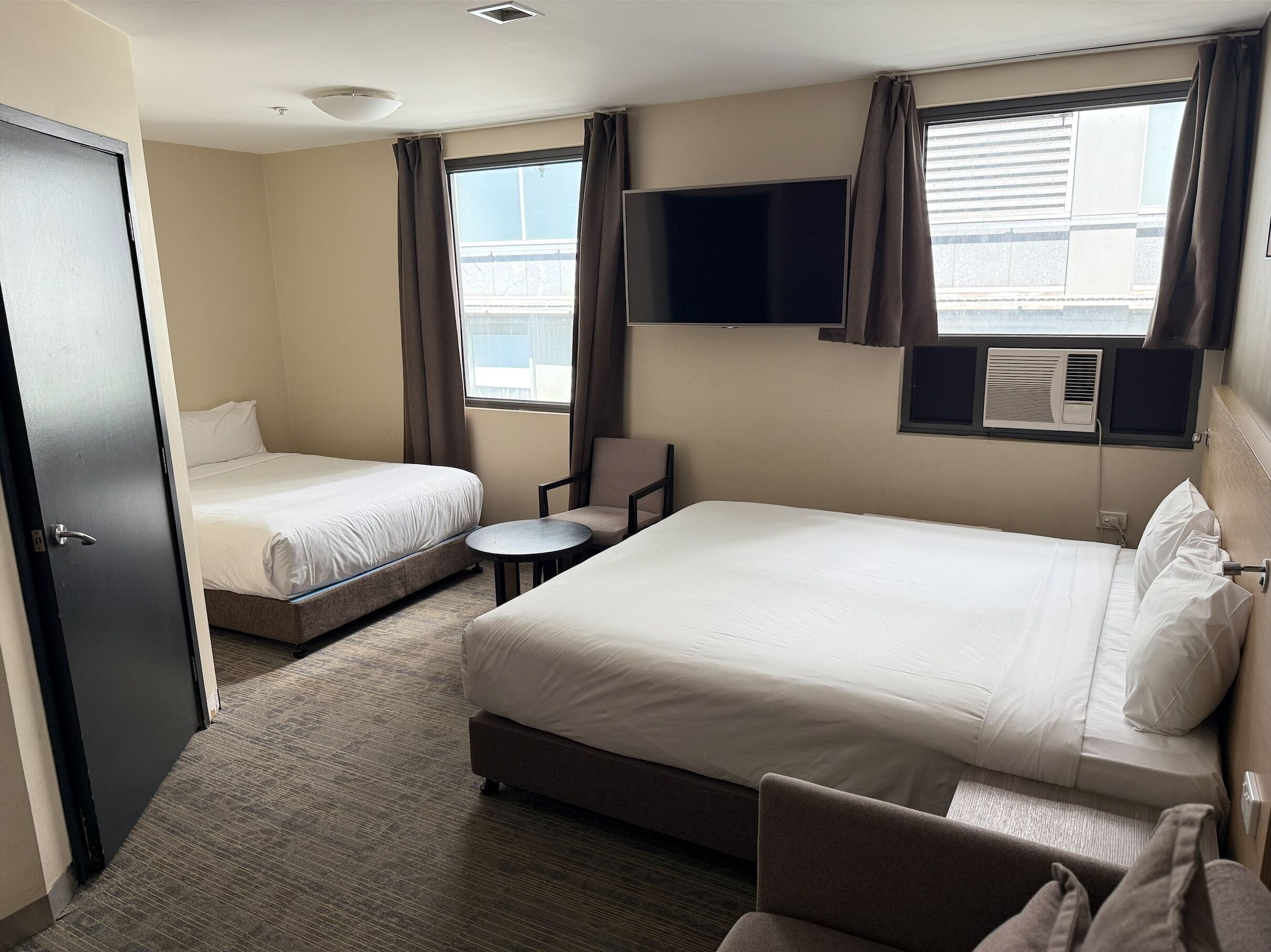 Habitación de hotel con dos camas individuales, una mesita pequeña, una silla, un televisor y un equipo de aire acondicionado.