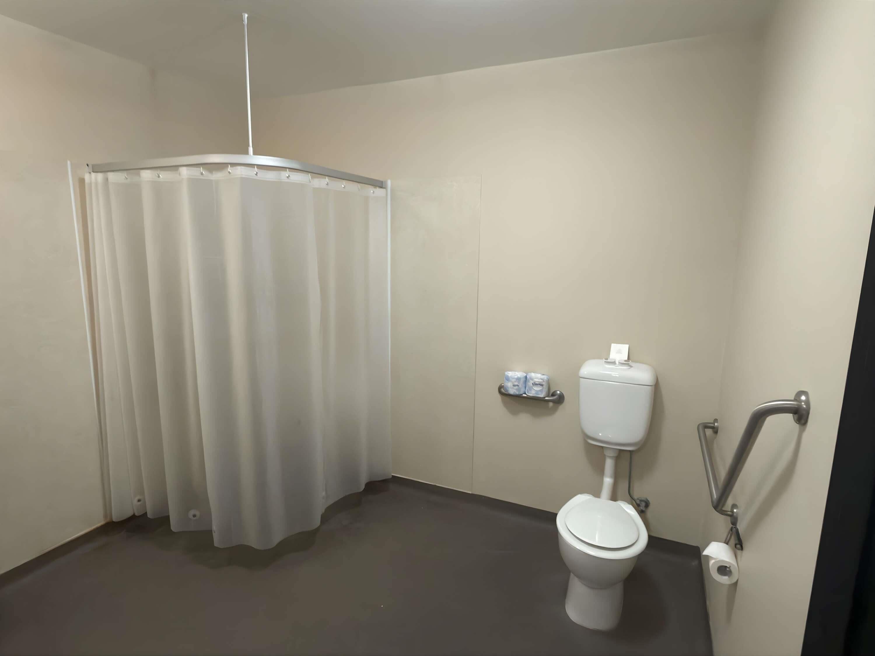 A small, private bathroom with a toilet, a shower curtain, a toilet paper holder, and a handrail.