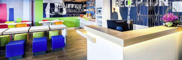 A modern restaurant with colorful stools, a counter, and a wall with various items displayed. - ibis budget Melbourne Airport (Melbourne Airport)
