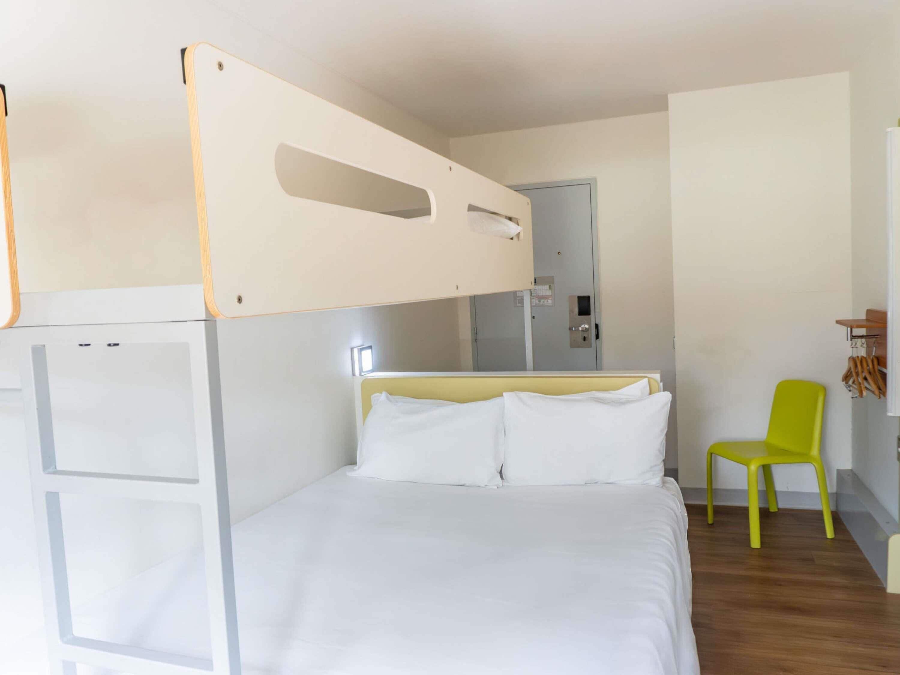 A room with a bunk bed, a single bed, a chair, and a small table.