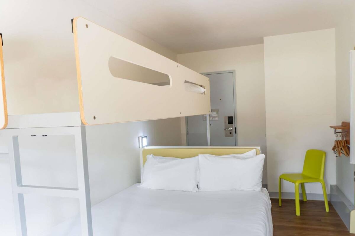 Una habitación de hotel con literas, una cama individual, una silla y una mesita.