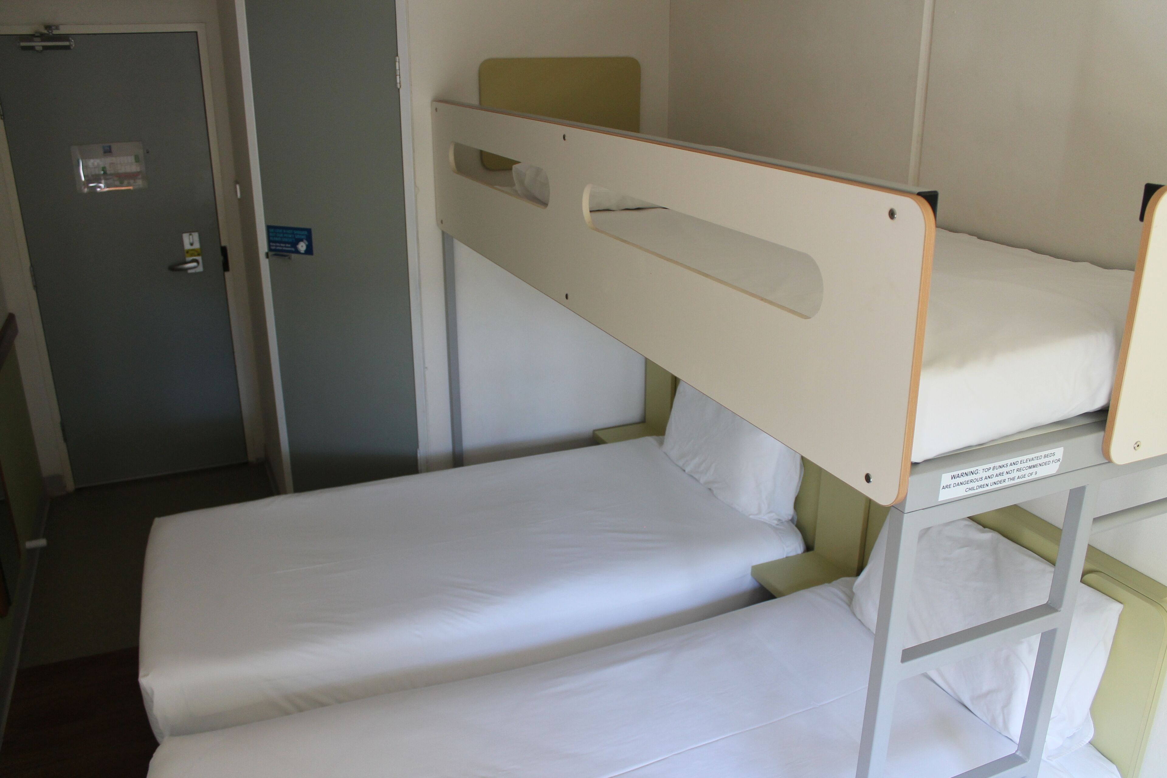 Una litera con ropa de cama blanca y una puerta con un letrero.