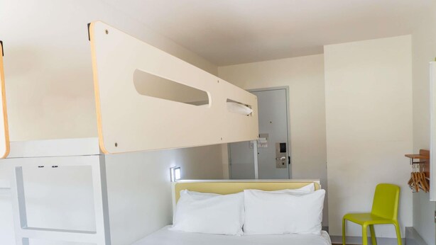 Een kamer met een stapelbed, een enkel bed, een stoel en een klein tafeltje.
