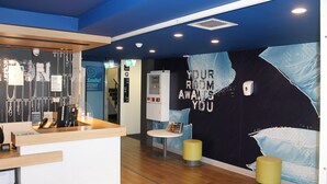 Un espace d’accueil comprenant un comptoir, une petite table et un mur où est affiché un message.