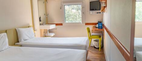Une chambre d’hôtel avec deux lits, une salle de bain avec un miroir et un lavabo, un téléviseur fixé au mur et une fenêtre laissant entrer la lumière naturelle.