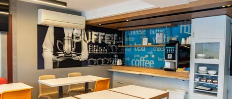 A modern cafe with tables, chairs, a coffee bar, and a wall with coffee-related words.