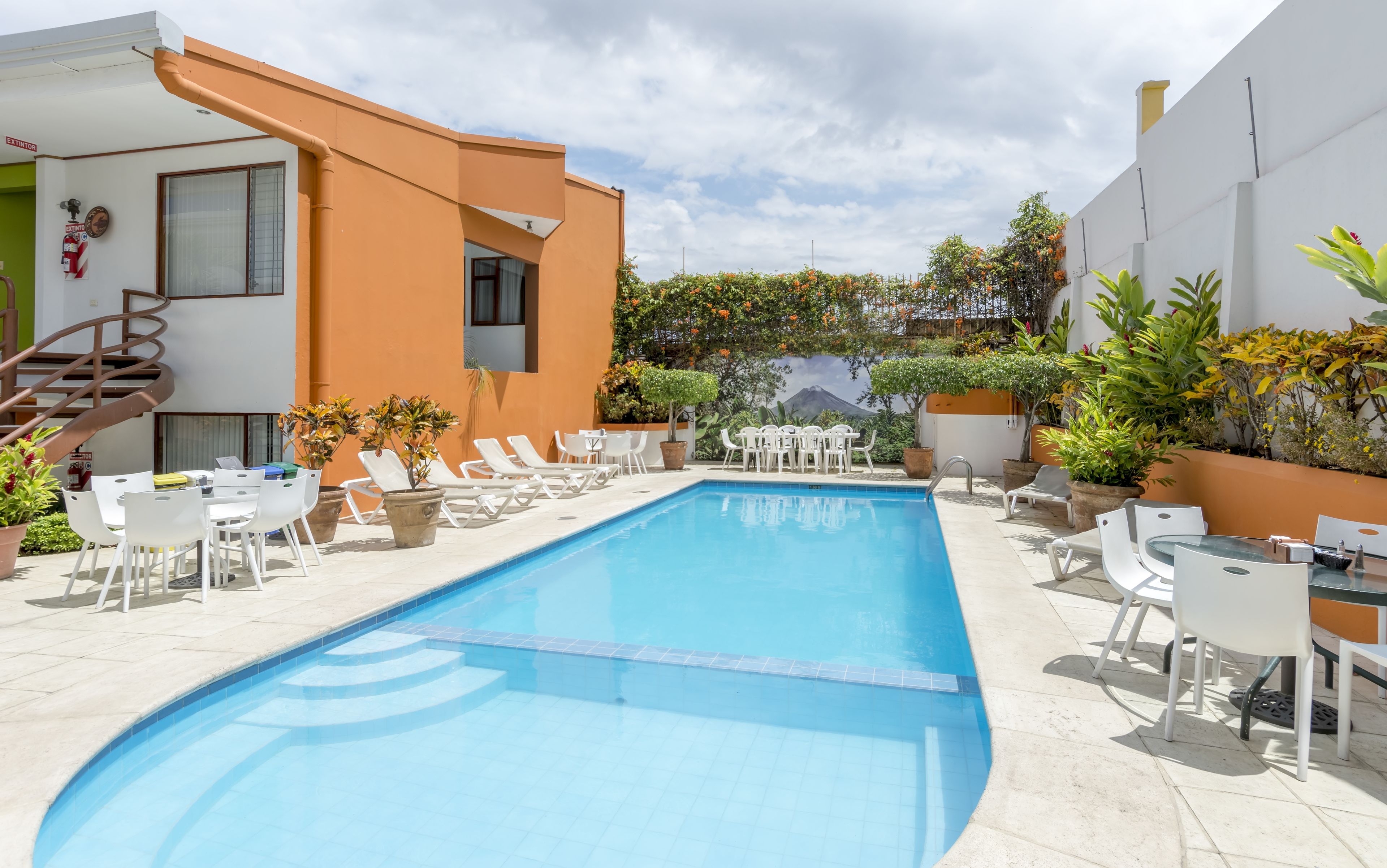A swimming pool with lounge chairs and tables, surrounded by potted plants and a staircase.