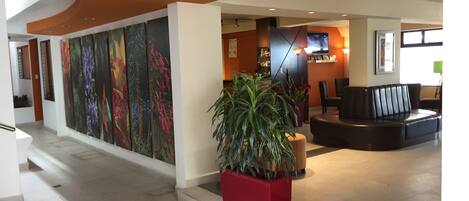A modern lobby with a curved ceiling, a reception desk, a seating area, and a large wall with floral artwork.