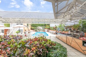An outdoor pool area with a covered seating area, a buffet station, and various plants. - Hotel Residence Inn Suites Cristina (San José)