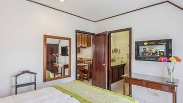 A hotel room with a bed, a mirror, a desk, a television, and a view into the kitchen.