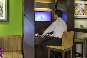 Un hombre sentado en un escritorio con un monitor de computadora mostrando el logotipo de Windows, en una habitación de paredes verdes y una obra de arte enmarcada a la izquierda.
