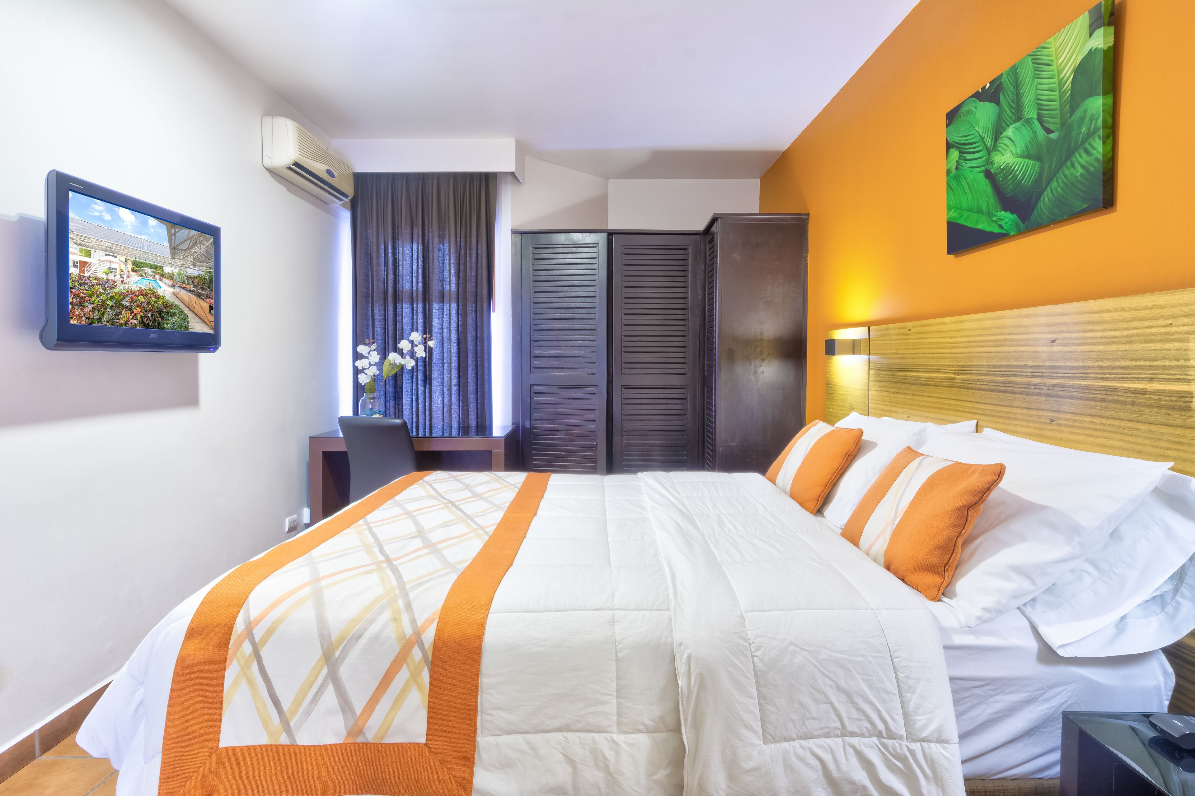 A hotel room with a bed, a desk, a chair, a wardrobe, and a picture on the wall.