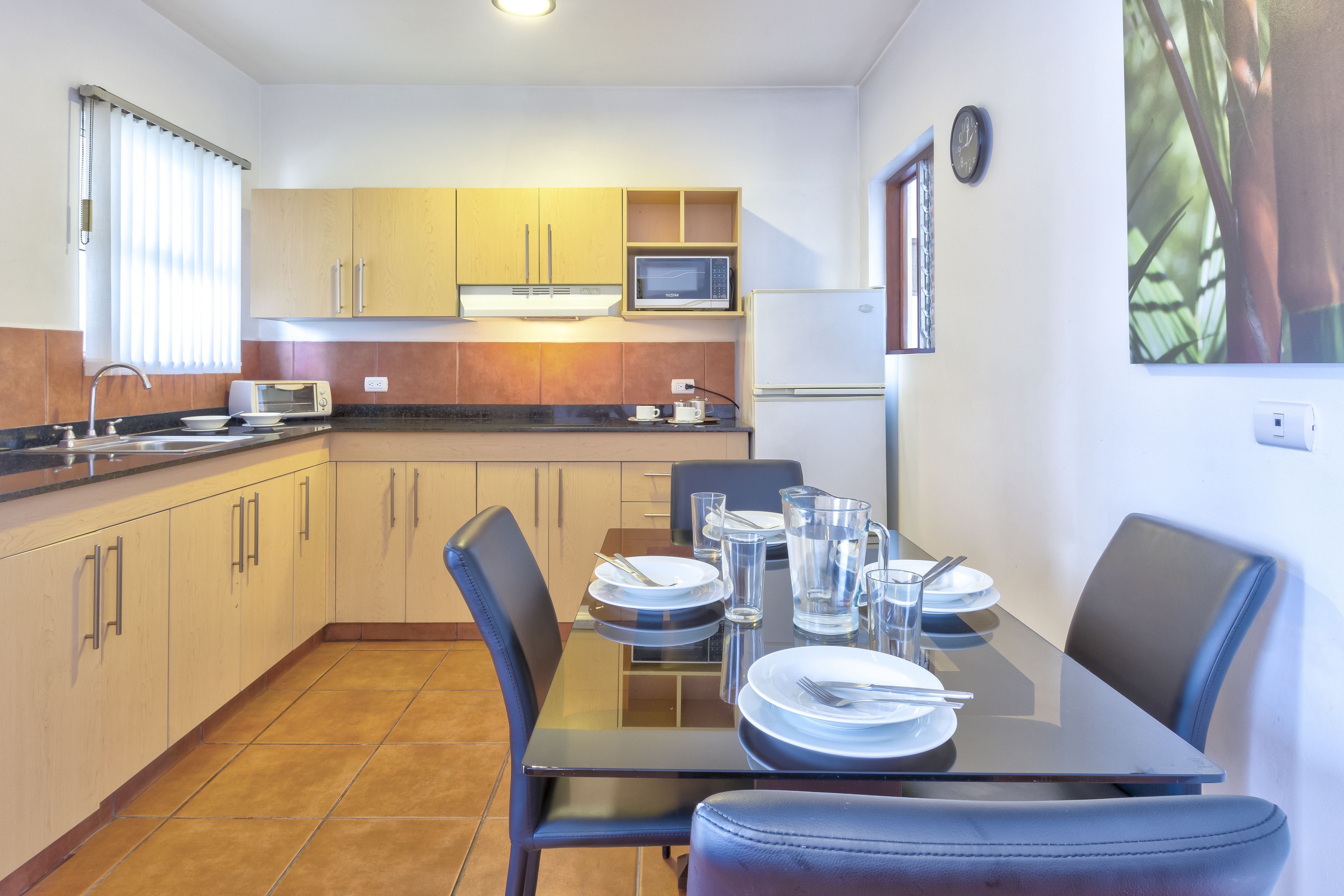 A modern kitchen with a dining table set for four, equipped with a microwave, toaster, and refrigerator.