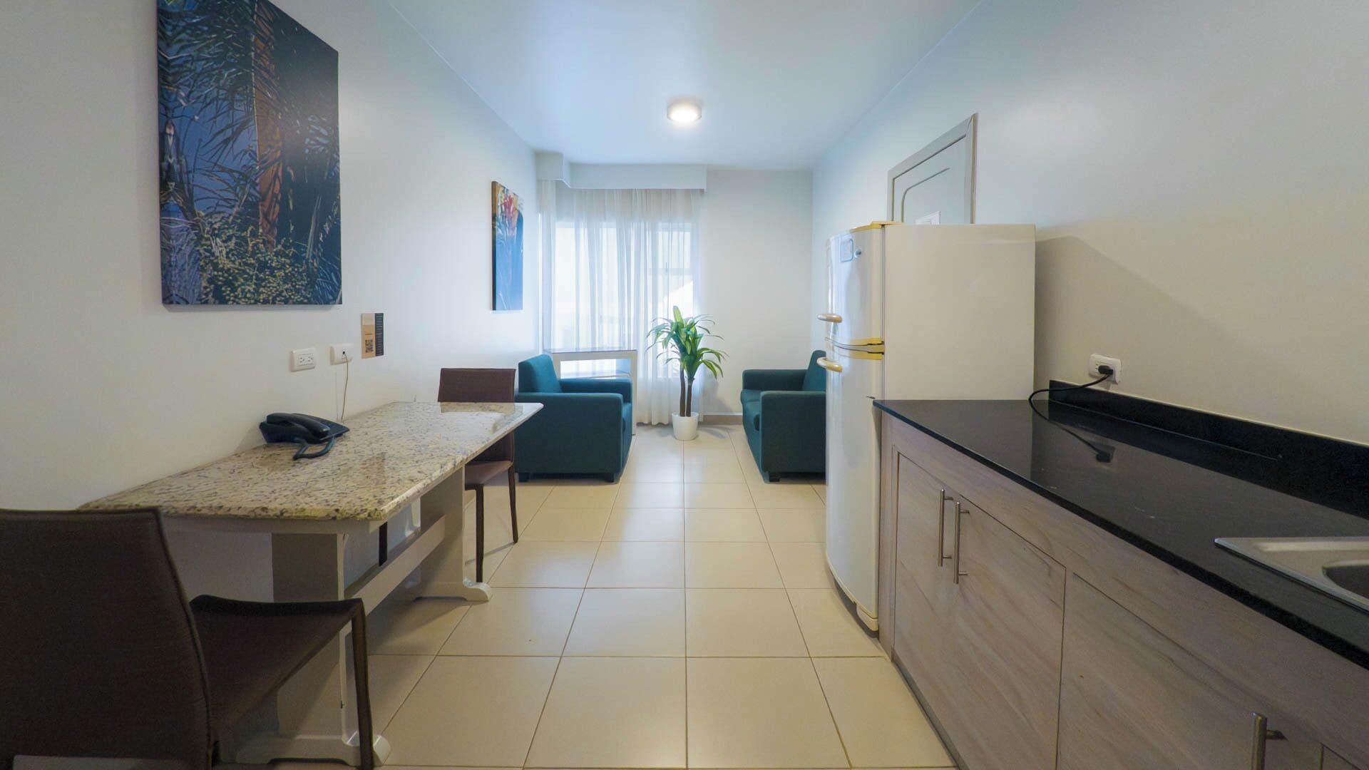 A modern kitchen with a granite countertop, a refrigerator, and a dining area with a table and chairs.