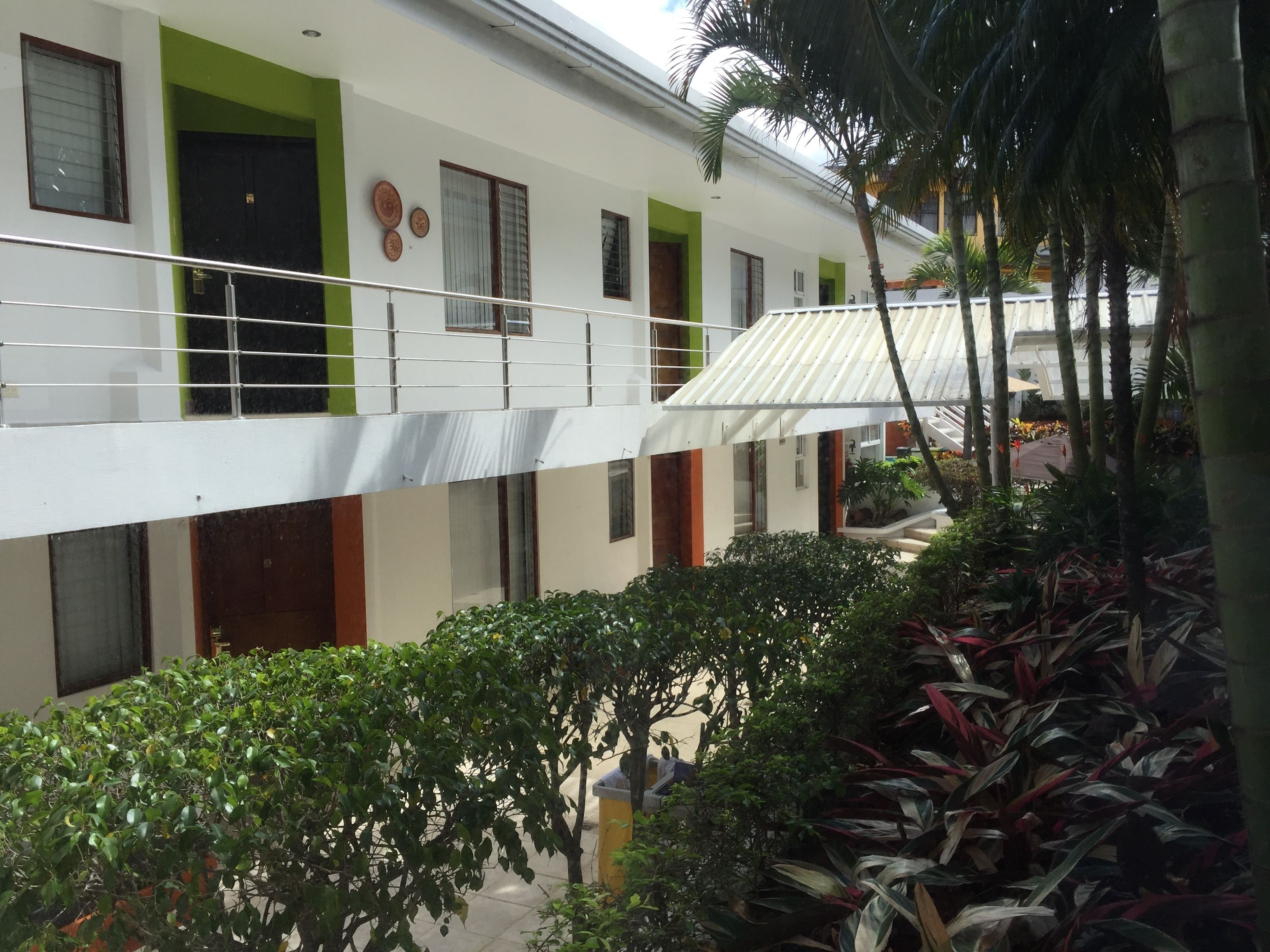 A multi-story building with balconies, green accents, and a covered outdoor area with plants.
