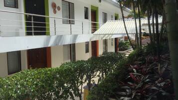 A multi-story building with balconies, green accents, and a covered outdoor area with plants.
