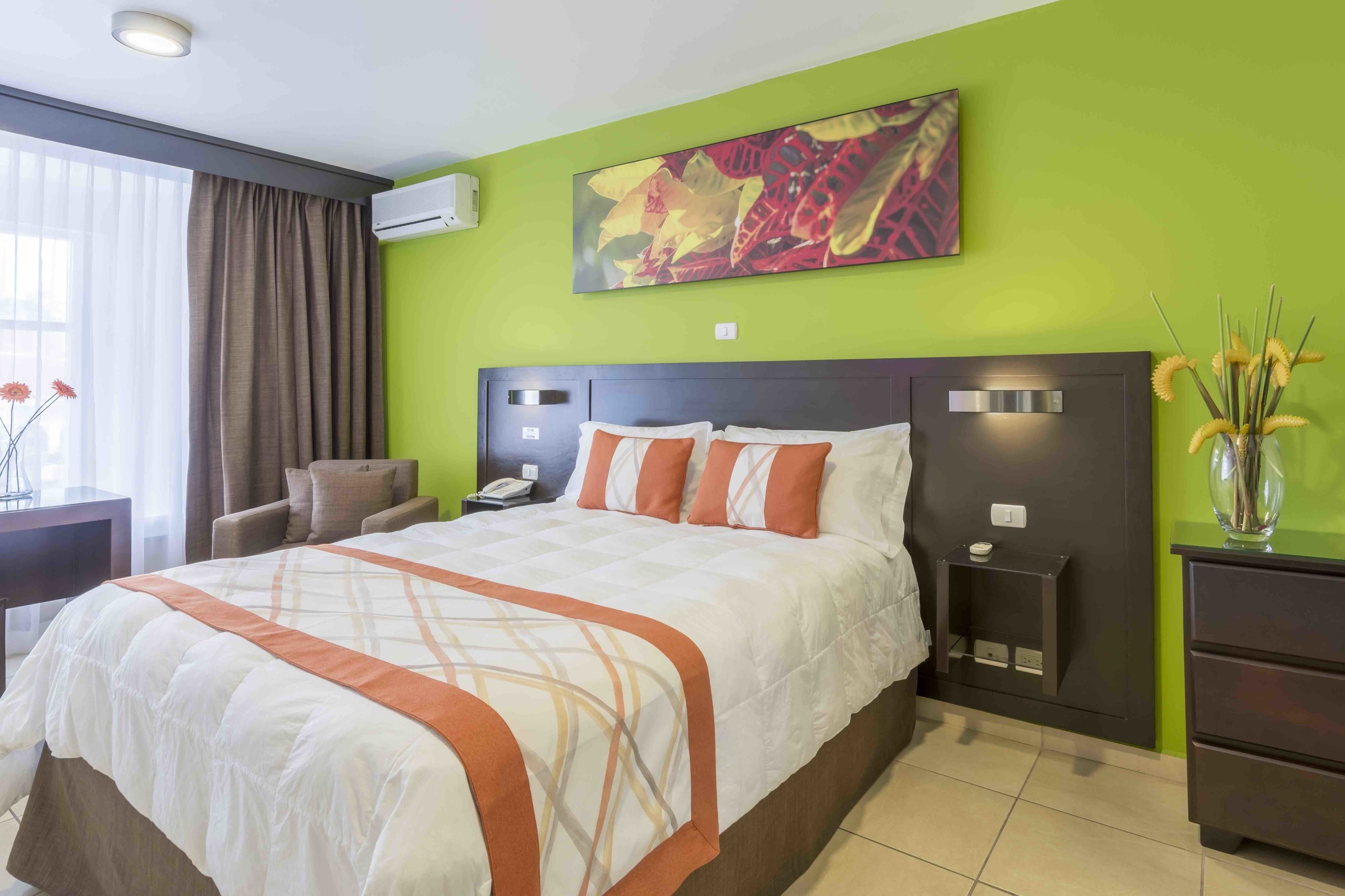 Habitación de hotel con una cama grande, una mesita de noche, un escritorio, una silla y un florero con flores.