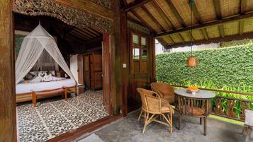 A room with a bed, a chair, and a table with a bowl of fruit.