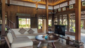 A wooden interior with a sofa, a round table, and a television. - Puri Tupai (Ubud)
