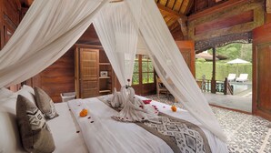 A bedroom with a canopy bed, a wooden door, and a view of a pool and garden. - Puri Tupai (Ubud)