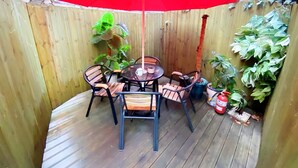 A wooden deck with a round table and chairs, a red umbrella, and potted plants. - Aroha Guest House (Seoul)