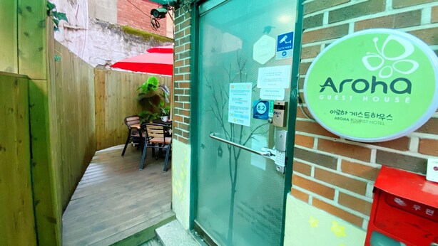 A hotel entrance with a glass door, a red umbrella, and a sign for Aroha Guest House. - Aroha Guest House (Seoul)