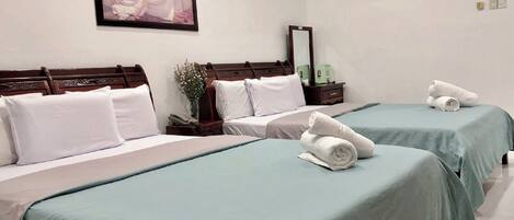 Habitación de hotel con dos camas, cada una con una colcha verde y almohadas blancas. Encima de las camas hay un cuadro enmarcado, una mesita de noche con una lámpara y una toalla doblada sobre la cama.