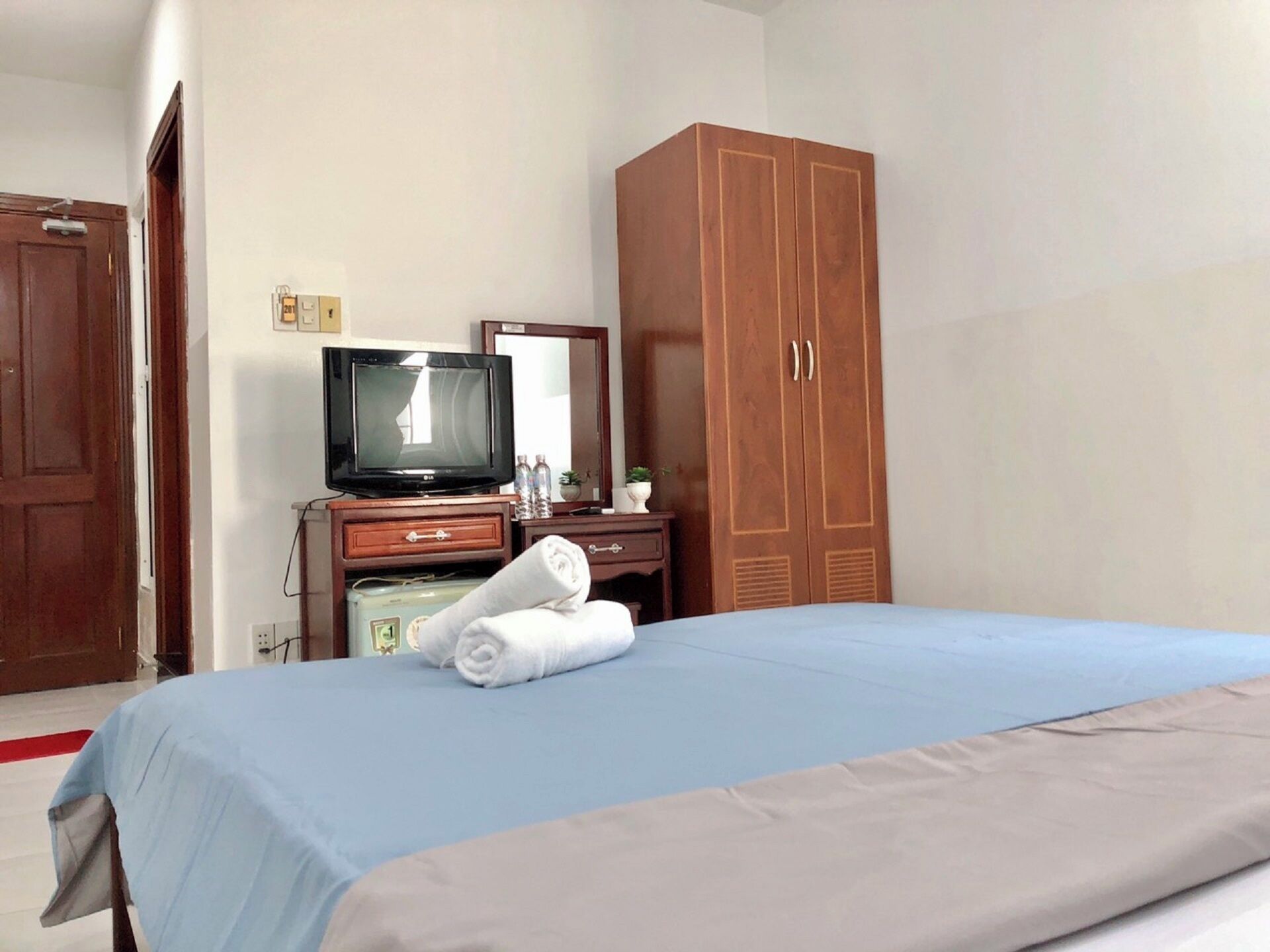 A hotel room with a bed, a wooden wardrobe, a television, and a mirror.