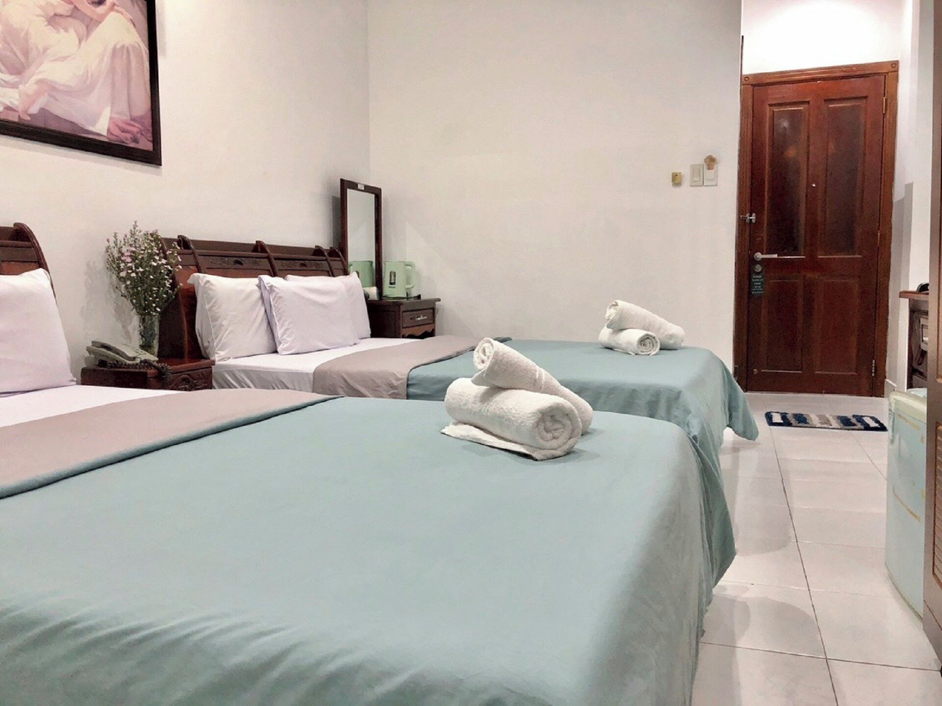 Habitación de hotel con dos camas, cabecero de madera, mesita de noche, espejo y una puerta.