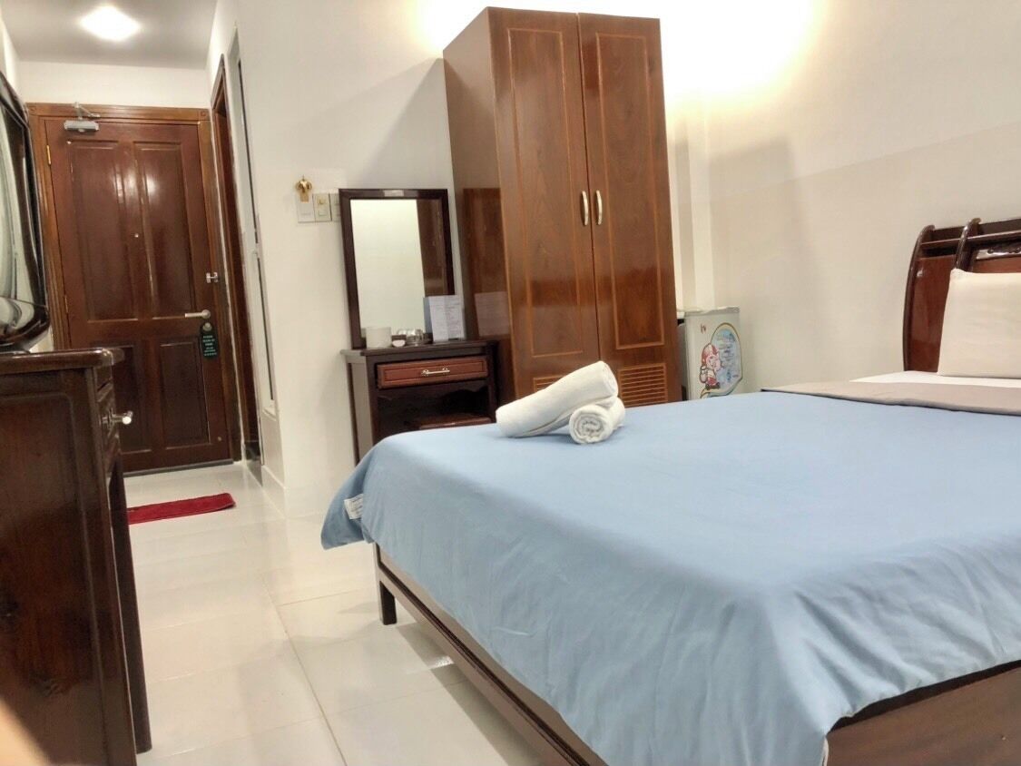 A hotel room with a bed, a wardrobe, a desk, a mirror, and a red carpet.