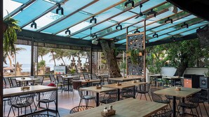 An outdoor dining area with wooden tables and chairs, a glass ceiling, and a view of the ocean. - Anantara Vacation Club Legian (Legian)