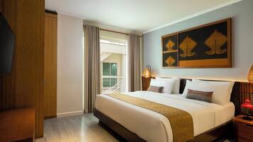 A hotel room with a large bed, a wooden wardrobe, a desk, and a window with curtains.